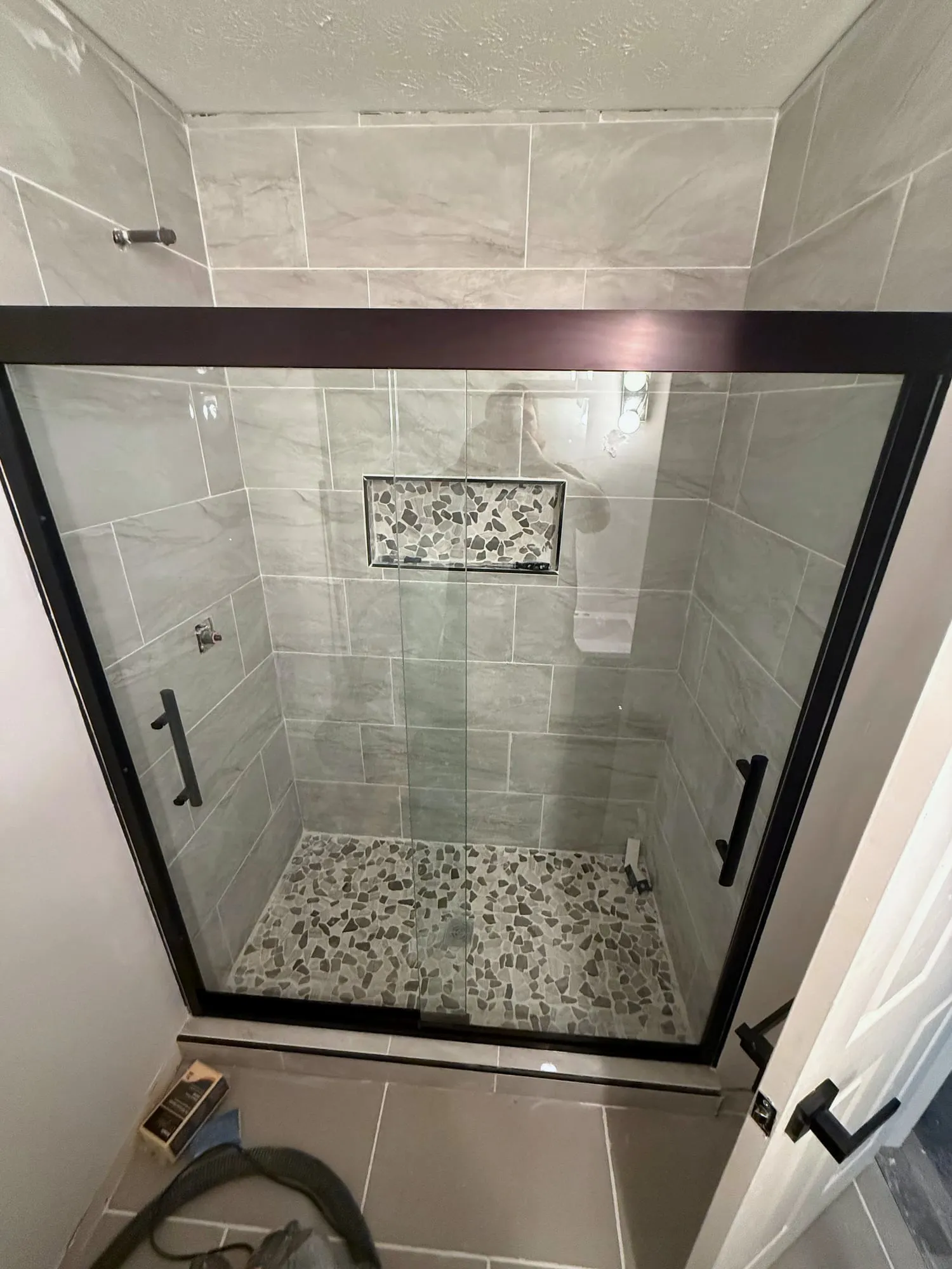 Tiled shower with black-framed sliding glass and a pebble floor