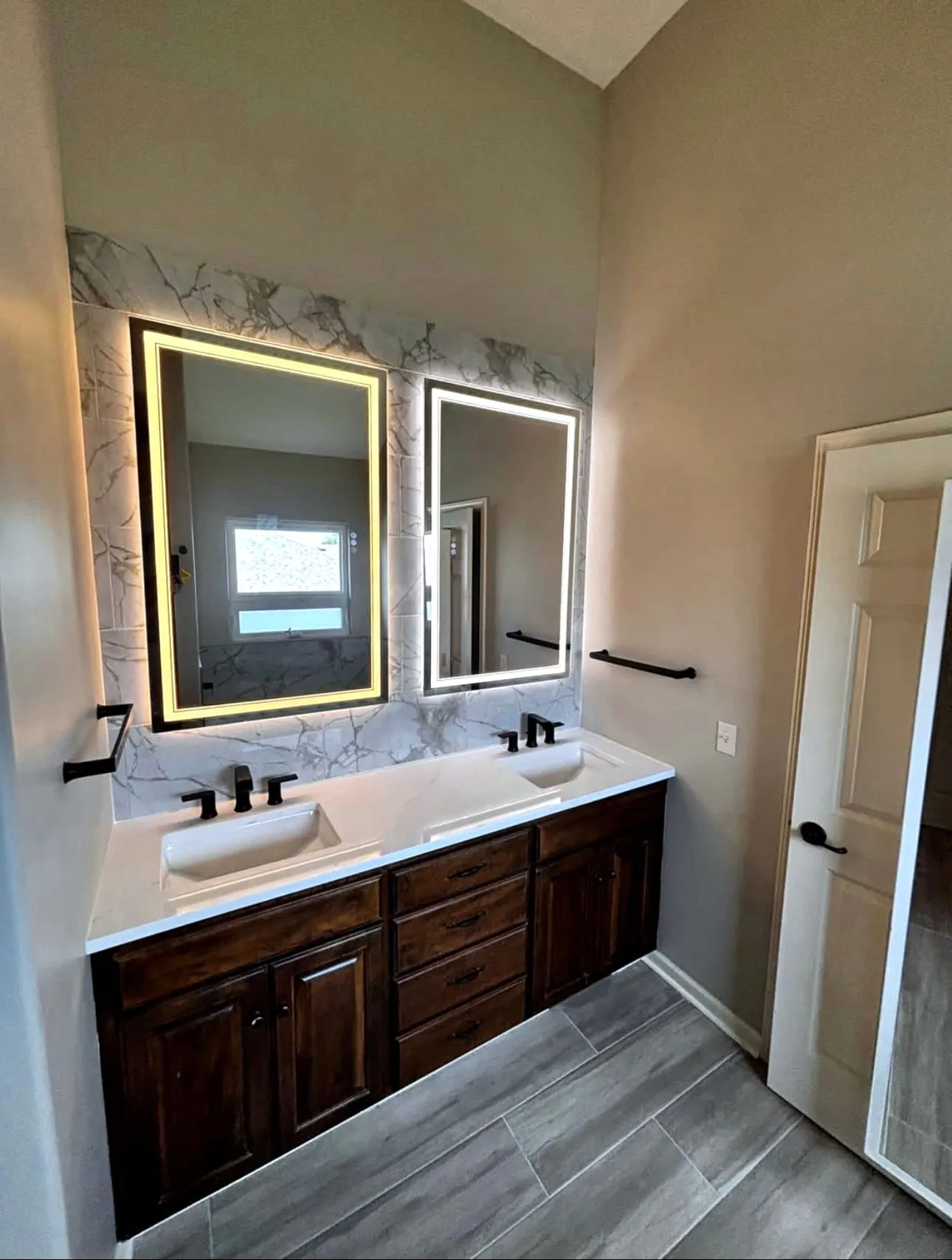 Double vanity with a marble-look backsplash and lighted mirrors