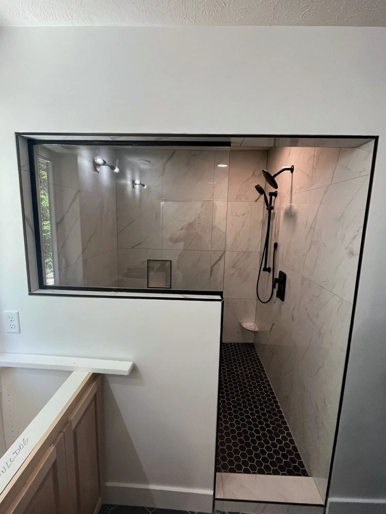 Walk-in shower with a half wall, black fixtures and hex tile floor