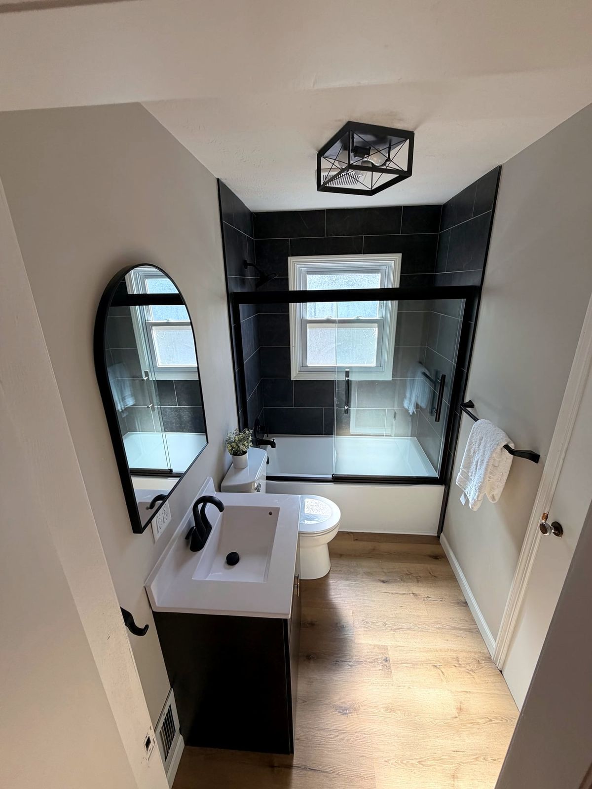 Remodeled bathroom with a black tile tub surround, black-framed glass, new vanity and an arched mirror