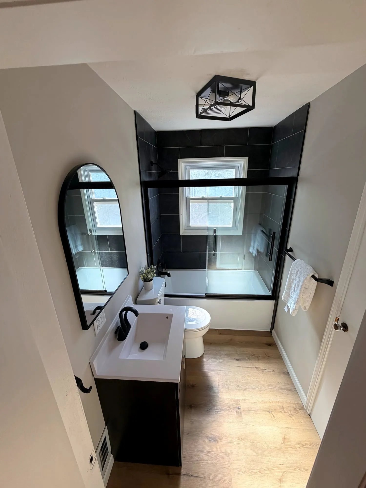 Remodeled bathroom with black tile, black-framed glass and an arched mirror