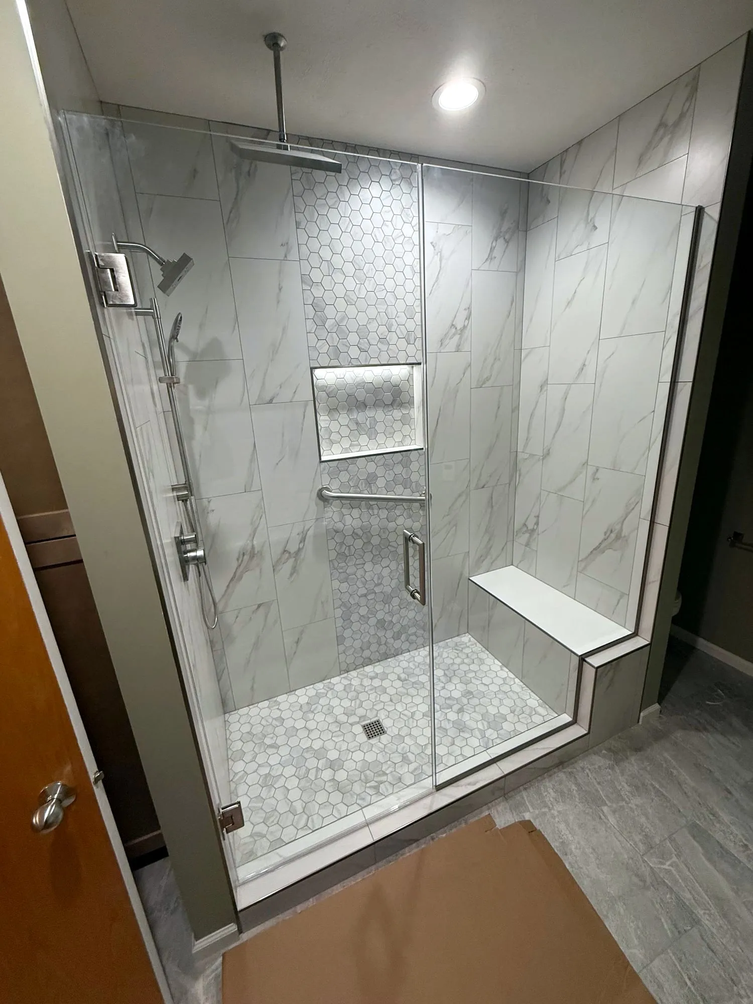 Shower with marble-look tile, a hex floor and a bench