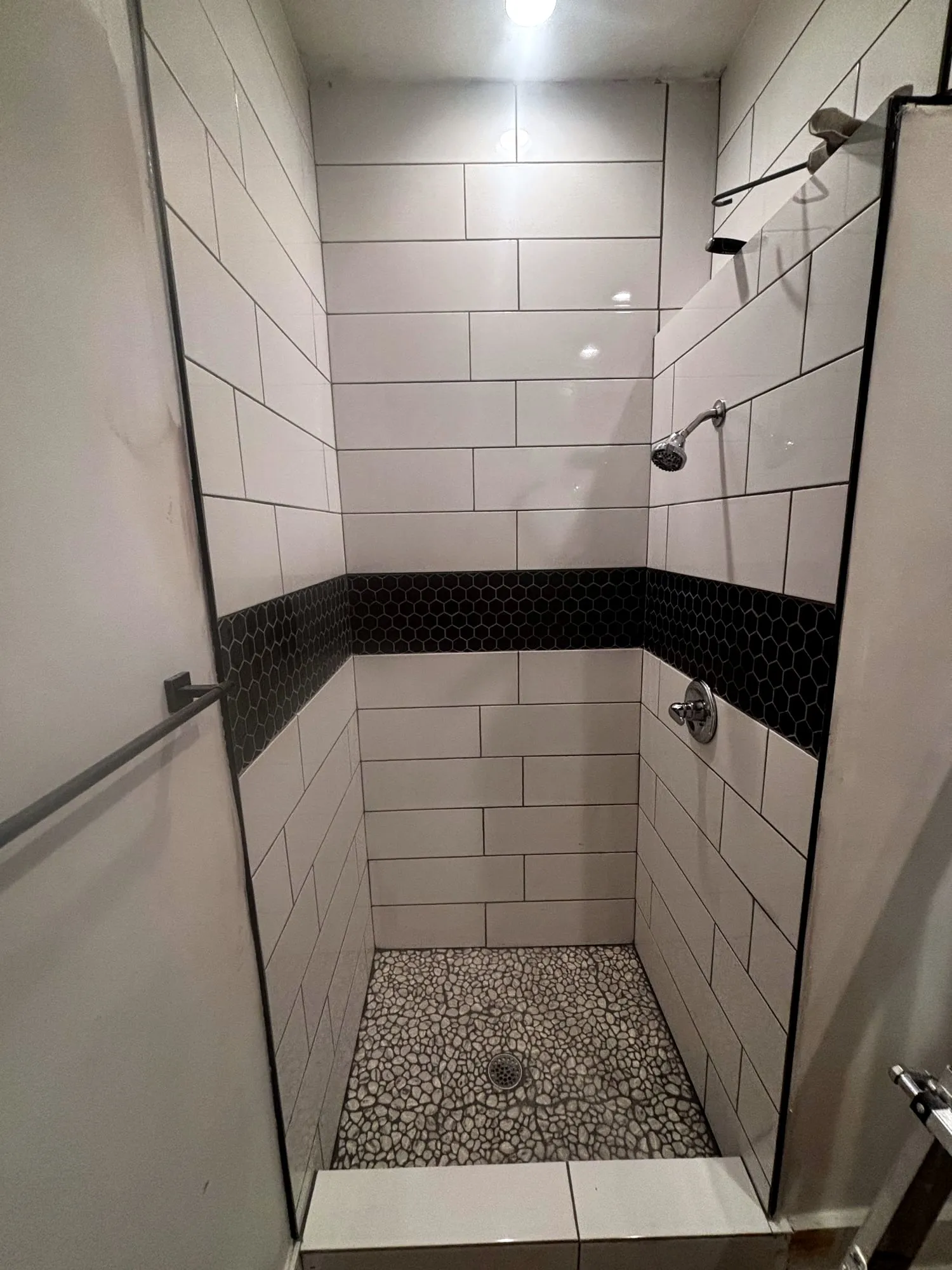 Walk-in shower with white subway tile, a black hex band and pebble floor