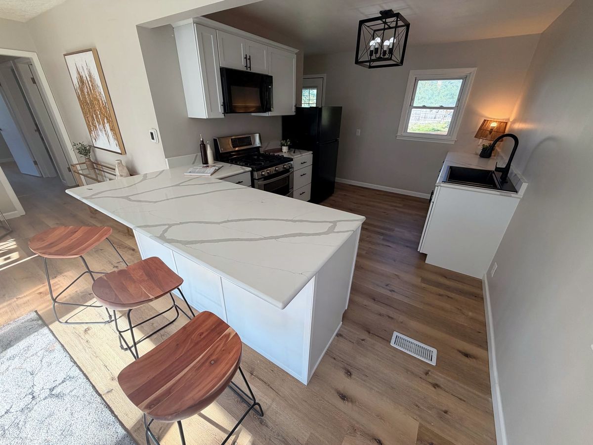 Remodeled kitchen with white cabinets, a quartz peninsula with stools and new flooring